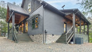 A two-story house with a stone foundation, wooden exterior, and a porch with stairs leading to the entrance. - Lake Views & Golf Access at Secluded Drasco Lodge (Drasco)