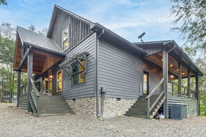 A two-story house with a stone foundation, wooden exterior, and a porch with stairs leading to the entrance. - Lake Views & Golf Access at Secluded Drasco Lodge (Drasco)