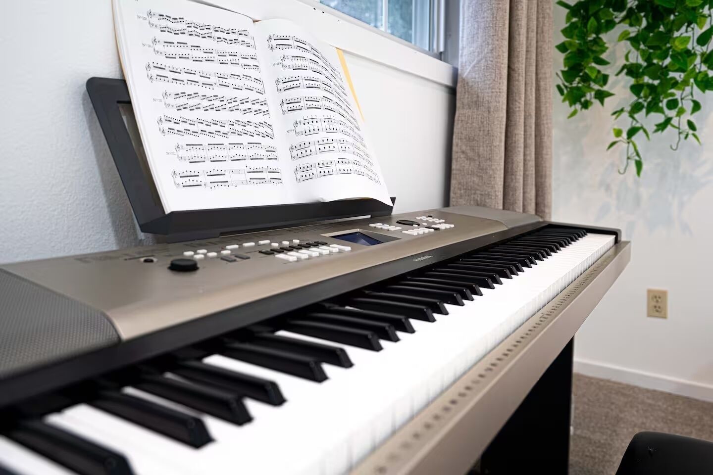 Un teclado con partituras sobre un atril, un control remoto y una planta al fondo.