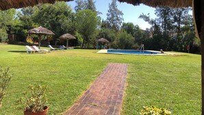 Un patio trasero con piscina, sillas de descanso y sombrillas de paja.