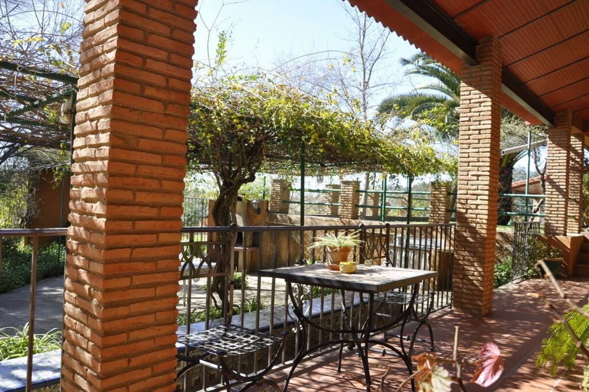 Een terras buiten met bakstenen pilaren, metalen hekwerk en een tafel met stoelen.