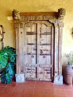 A rustic wooden door with intricate carvings and two lion heads on top, flanked by large plants and a potted plant. - Cortijo Zalamea  (Zalamea la Real)