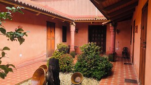Un patio con piso de baldosas, una puerta de madera y un pequeño jardín con plantas y un tocón de árbol.