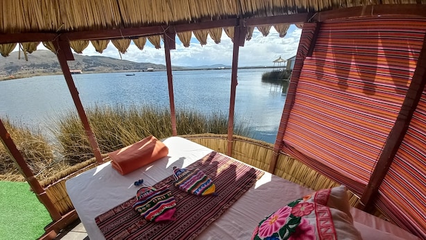 A bed with a white sheet, a colorful woven blanket, and a pink pillow with floral embroidery. - INTI TITIKAKA (Puno)