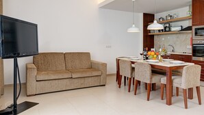 A modern living room with a sofa, dining table, chairs, a TV, and a kitchen area with appliances.