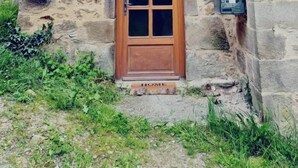 A stone building with a wooden door and shutters, a green sign indicating a guesthouse, and a welcome mat at the entrance. - Gîtes de France® - Au Refuge des Artistes (VIAZAC)