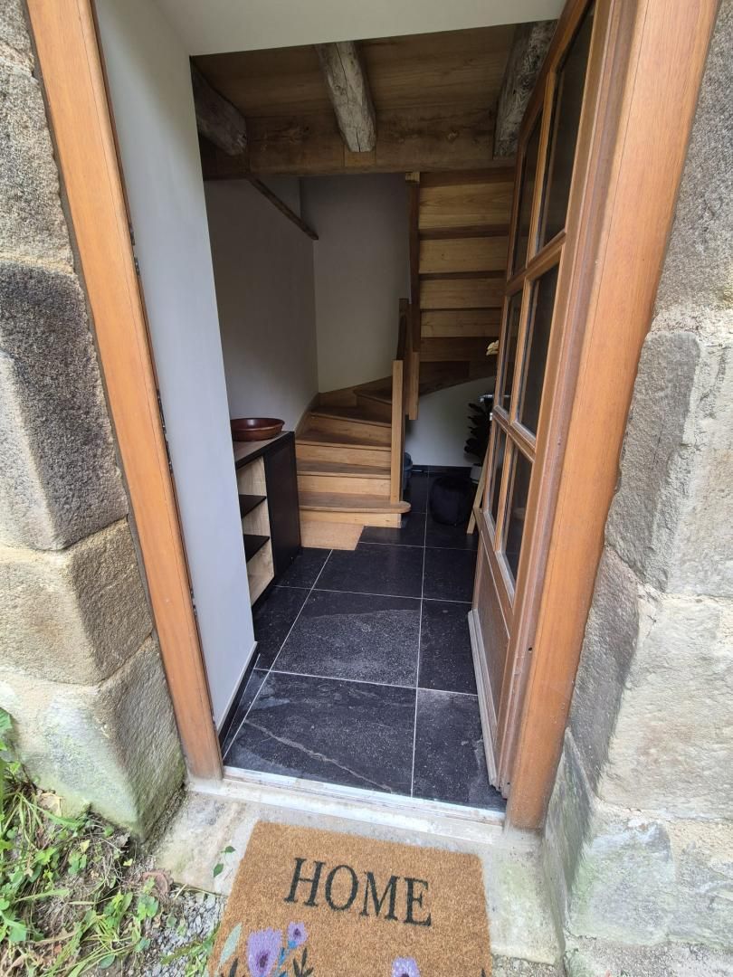 Une entrée aux murs de pierre, avec un escalier en bois menant à l’intérieur.