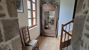 A room with stone walls, wooden flooring, a wooden chair, a table, a mirror, and a staircase. - Gîtes de France® - Au Refuge des Artistes (VIAZAC)