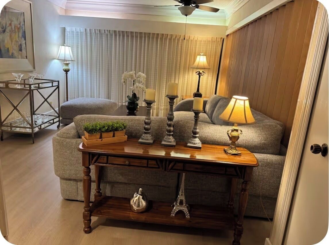 A living room with a sofa, a wooden coffee table with decorative items, a lamp, and a ceiling fan.