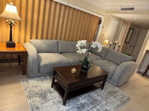 Una sala de estar con un sofá gris, una mesa de centro de madera oscura, una lámpara y un florero con flores.