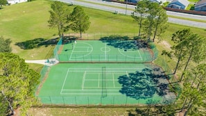 Luchtbeeld van een tennisbaan, omgeven door bomen en een weg.