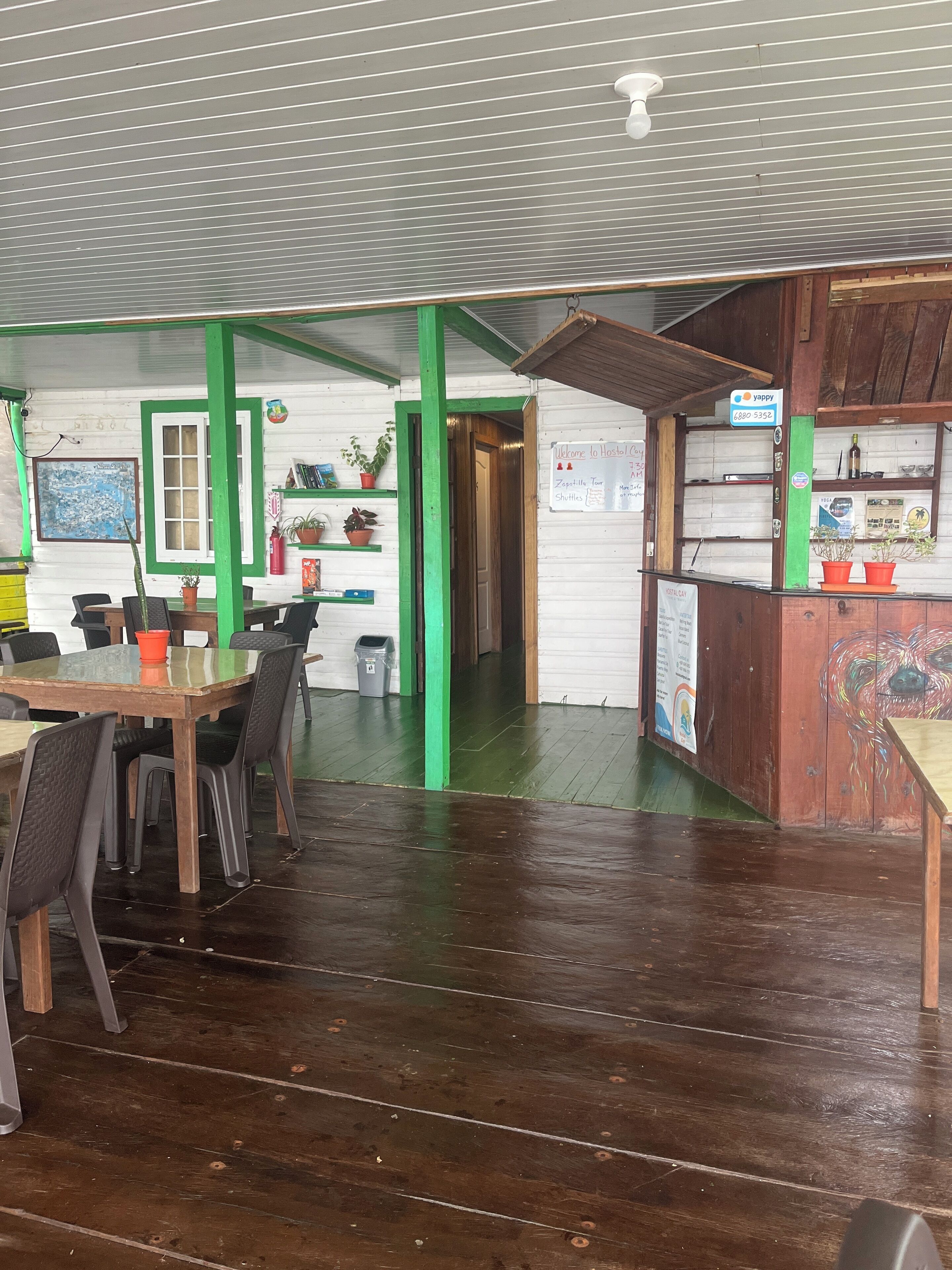 A hostel interior with a dining area, a reception desk, and a wooden floor.