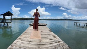 A wooden pier extending into a calm body of water with a person standing on a yoga mat. - Hostal Cay (Bastimentos)