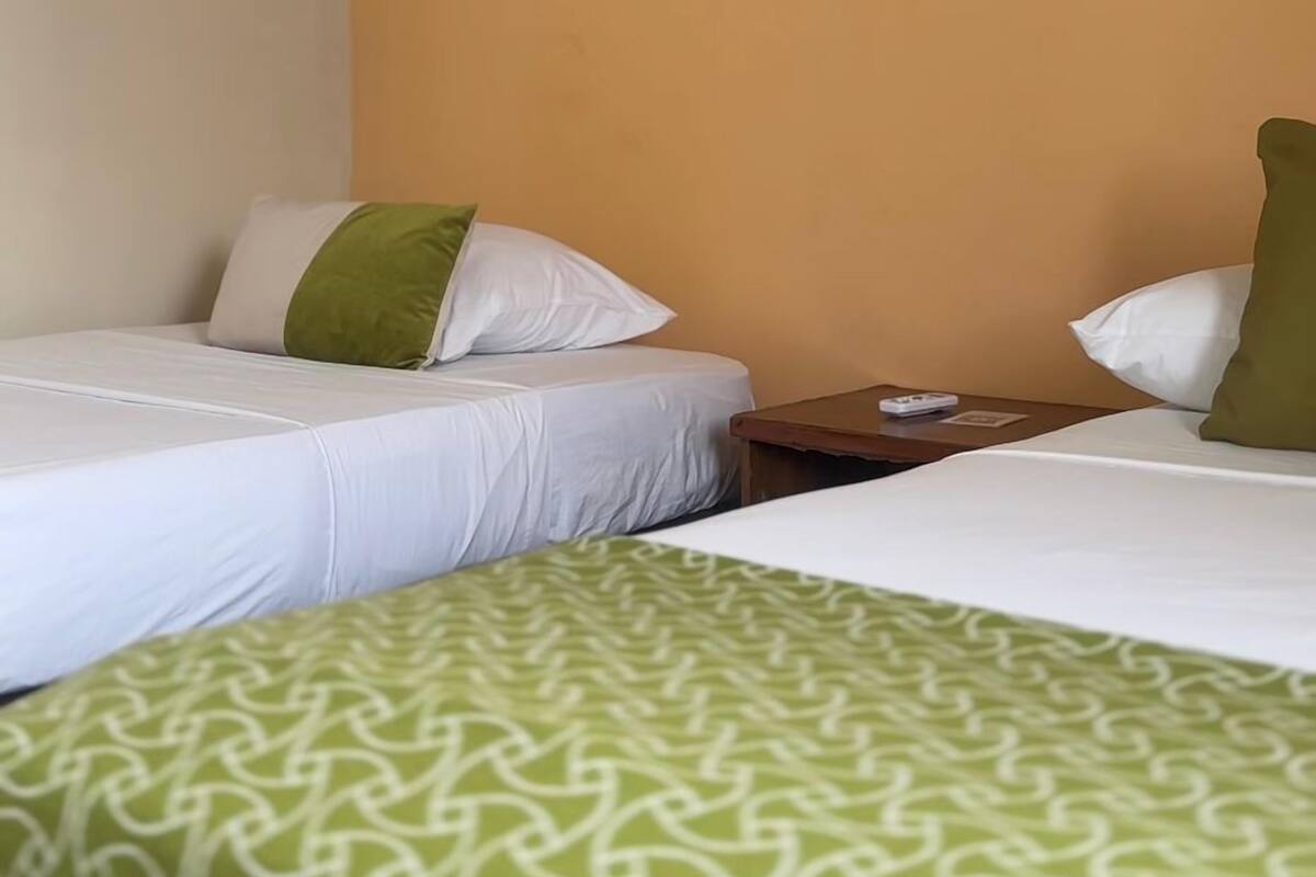 A hotel room with two beds, a small table, and a wall-mounted painting.