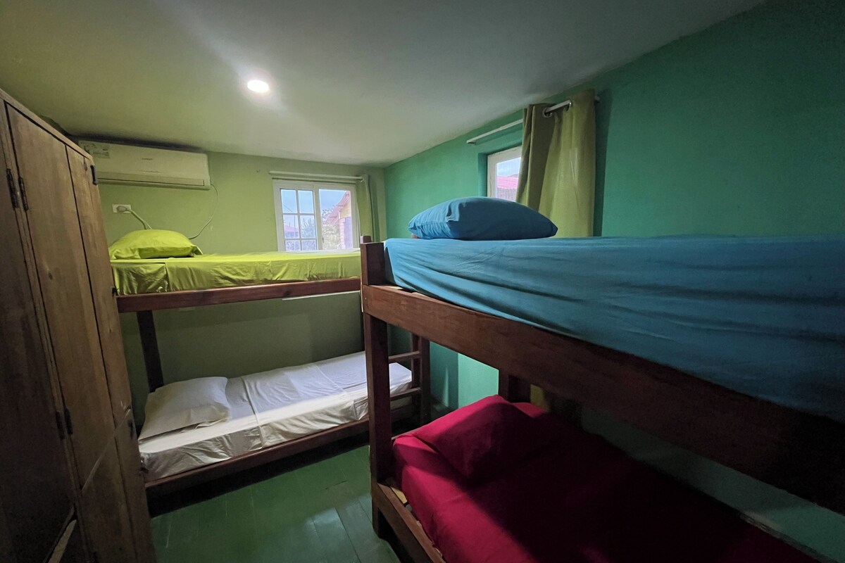 Une chambre de dortoir avec des lits superposés, une fenêtre et un luminaire au plafond.