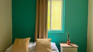 A bedroom with a bed, two pillows, a nightstand with a plant, and a window with curtains. - Hostal Cay (Bastimentos)