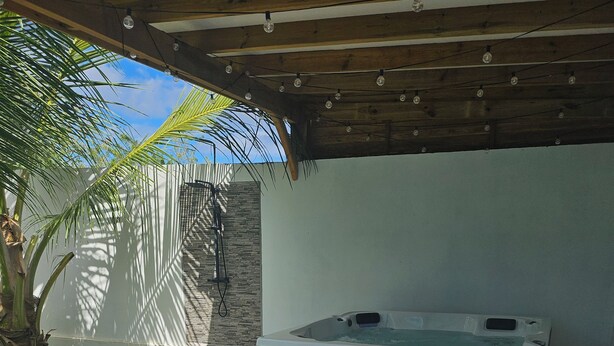 A covered outdoor area with a hot tub, white wicker furniture, and a stone wall.