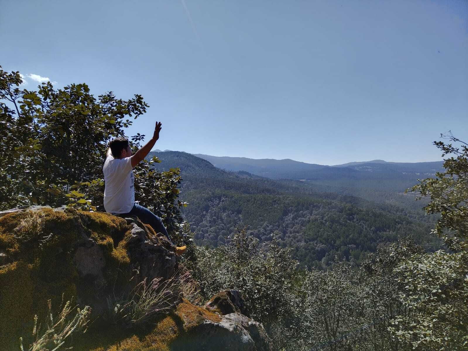 Una persona sentada sobre una roca con vistas a un valle y montañas.