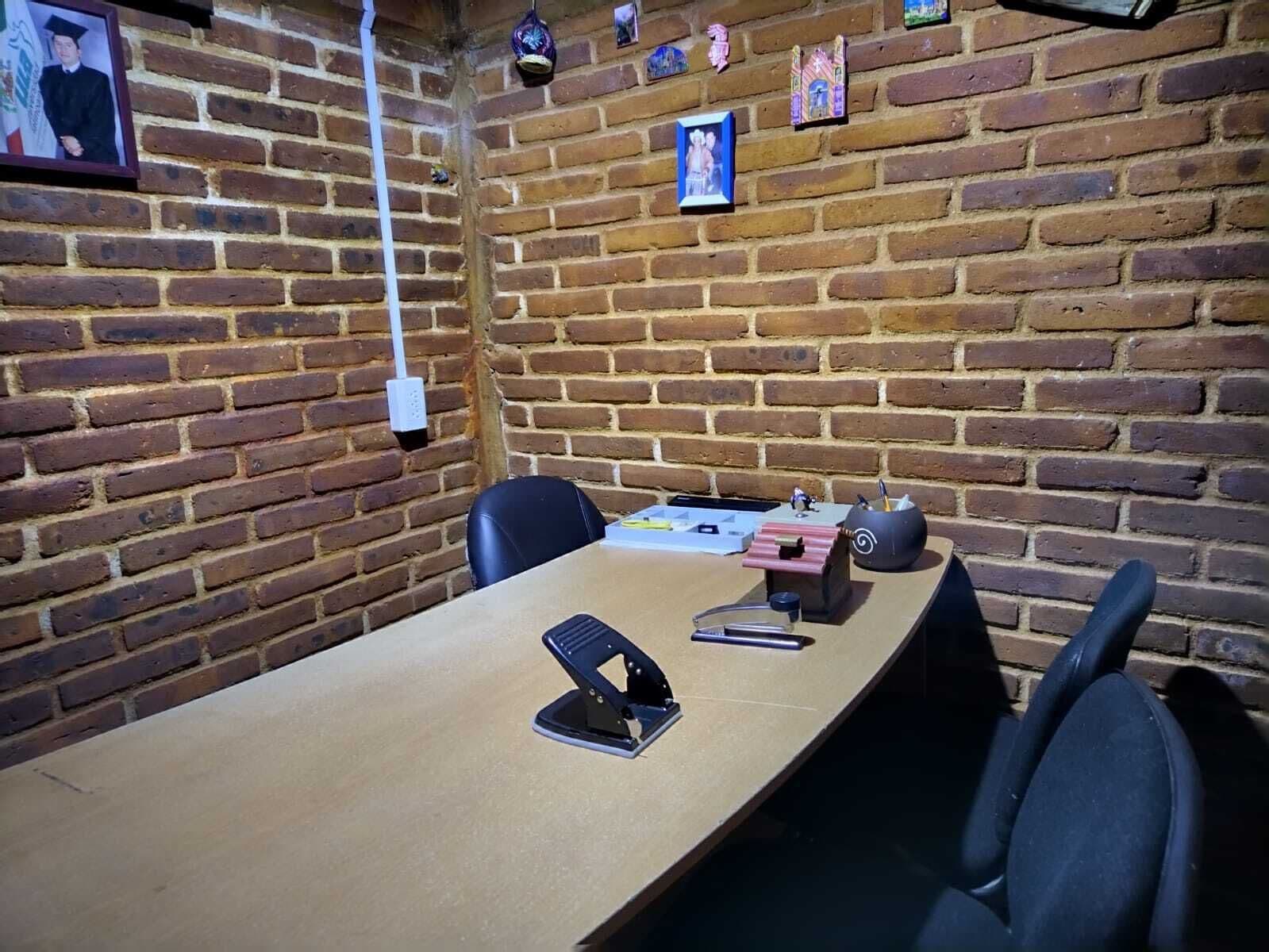 A conference room with a brick wall, a long table, and black office chairs.
