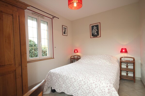 A bedroom with a bed, two bedside tables with lamps, a window, and two framed pictures on the wall.
