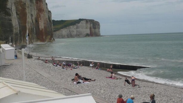 A pebble beach with people sunbathing and swimming, overlooking cliffs and the sea.