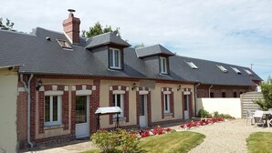 A two-story house with a brick exterior, multiple windows, and a small garden area with a table and chairs.