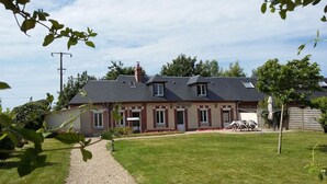 A two-story house with a gravel driveway, a lawn, and a garden with red flowers.