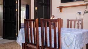 A dining area with a table set for four, wooden chairs, a clock on the wall, and a TV mounted above the table. - APARTMENT EL JOBO, LA CRUZ, AT 700 MTRS COPAL BEACH, 8 MIN FROM RAJADA (Provincia de Guanacaste)