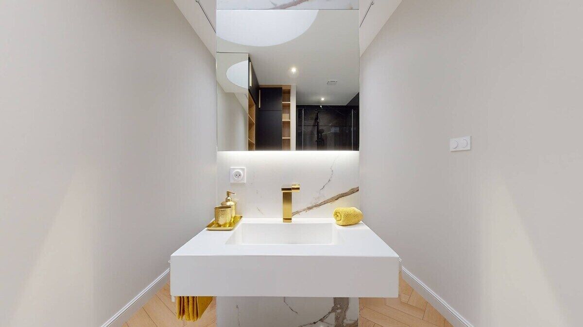 A modern bathroom with a white vanity, gold fixtures, and a large mirror.