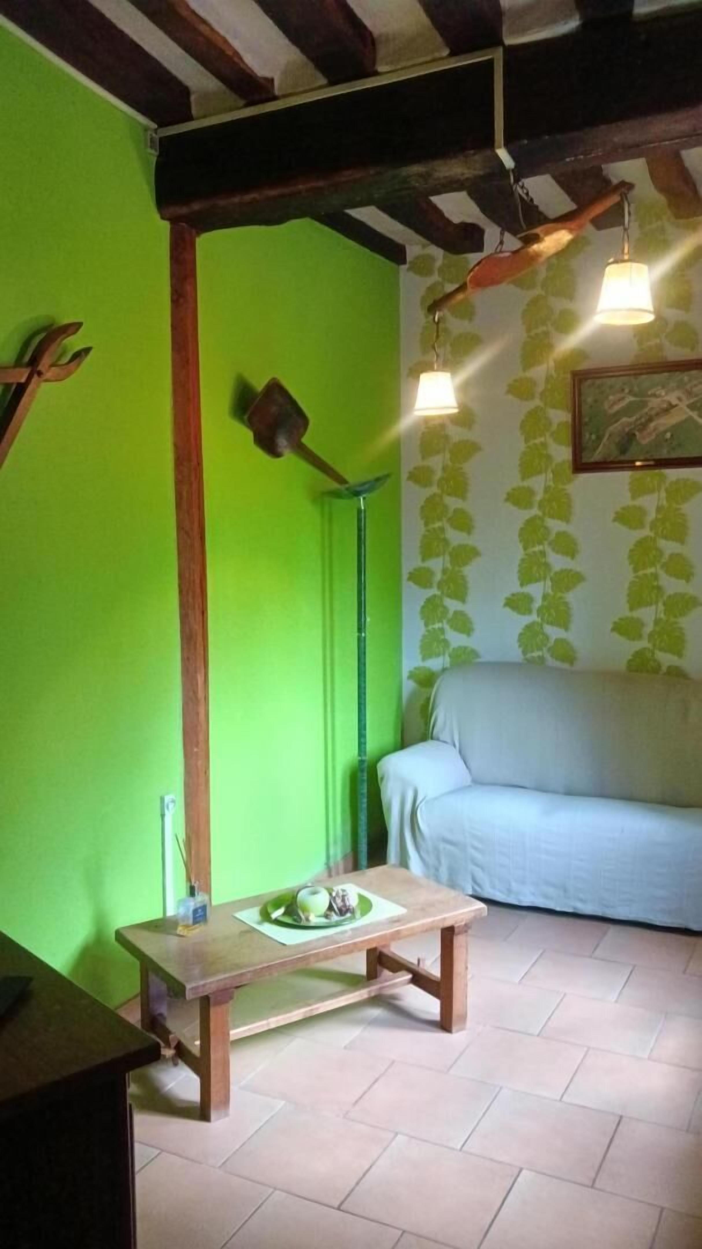 Een kamer met een groene wand, een houten tafel met eten erop, een lichtkleurige bank en een hanglamp.