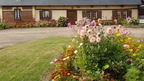 Ein zweistöckiges Haus mit geneigtem Dach, zahlreichen Fenstern und einem gepflegten Garten mit verschiedenen Blumen und Sträuchern.