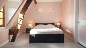 Ein Schlafzimmer mit schrägverdeckter Decke, einem Bett, zwei Nachttischen mit Lampen und einer Tür.