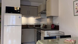 Una cocina compacta con refrigerador, microondas, horno y lavamanos. Hay una mesa de comedor con sillas y una alfombra estampada.