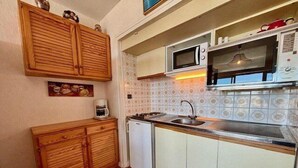 A compact kitchen with wooden cabinets, a microwave, a sink, and a small refrigerator.