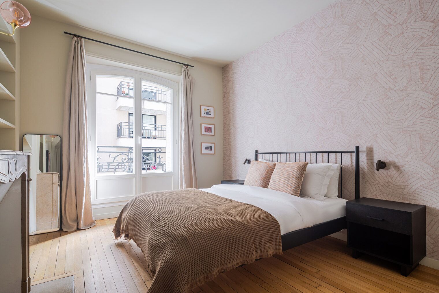 A bedroom with a bed, bedside table, and a view of balconies through a window.