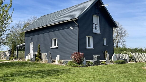A two-story house with a dark exterior, a sloped roof, and a small front porch. - Gîtes de France® - l'Humesnil (ST VICTOR L'ABBAYE)