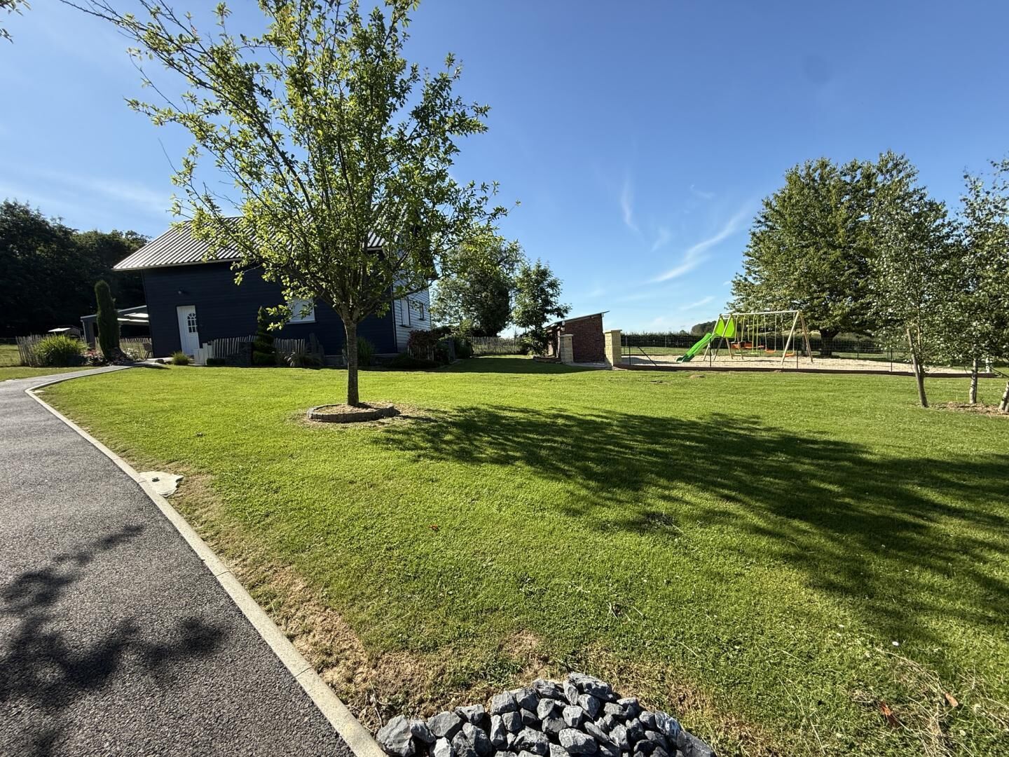 Een woonwijk met een verzorgd gazon, een speeltuin en een huis met een donkere gevel.