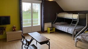 A dormitory room with bunk beds, a desk, a chair, a table, a TV, and a large window with a view of a green field. - Gîtes de France® - l'Humesnil (ST VICTOR L'ABBAYE)