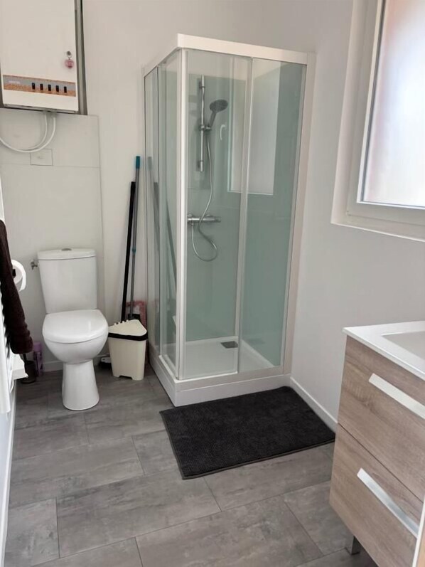 Un baño moderno con ducha envuelta en vidrio, inodoro blanco y tocador de madera.