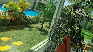 Vista desde una ventana sobre una piscina, un área con césped y un edificio con tejado de baldosas.
