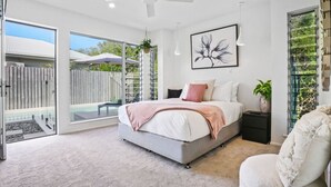 A modern bedroom with a large bed, a ceiling fan, and a view of the outdoors.