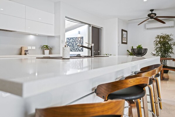 Una cocina moderna con una isla grande, taburetes de madera y un ventilador de techo.