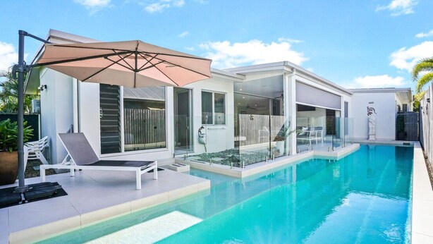 A modern poolside area with a clear blue pool, a lounge chair, and a large umbrella.