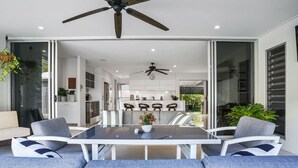 A modern living room with a glass dining area, a ceiling fan, and a view of the kitchen and dining area.