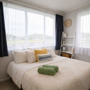 Un dormitorio con cama, almohadas, una toalla verde, un reloj y vistas al exterior.