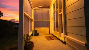 A covered porch with a door, a small step, and a potted plant. - The Coasty Bach | Cosy Cottage | Rest & Reset (Tolaga Bay)
