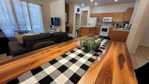 A modern living room with a wooden dining table, checkered rug, and a kitchen area with wooden cabinets and appliances. - Bella Vida Home (Kissimmee)