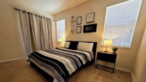 A bedroom with a bed, curtains, a nightstand, wall art, and a window. - Bella Vida Home (Kissimmee)