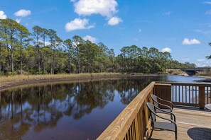 A wooden deck with chairs overlooking a calm body of water, surrounded by trees. - Redfish Village M2-329 - 3BR/3BA Corner Condo - Sleeps 12 - Community Pool (Blue Mountain Beach)