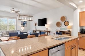 Una cocina moderna con encimeras de granito, lavavajillas y una zona de comedor con sofá y sillas.